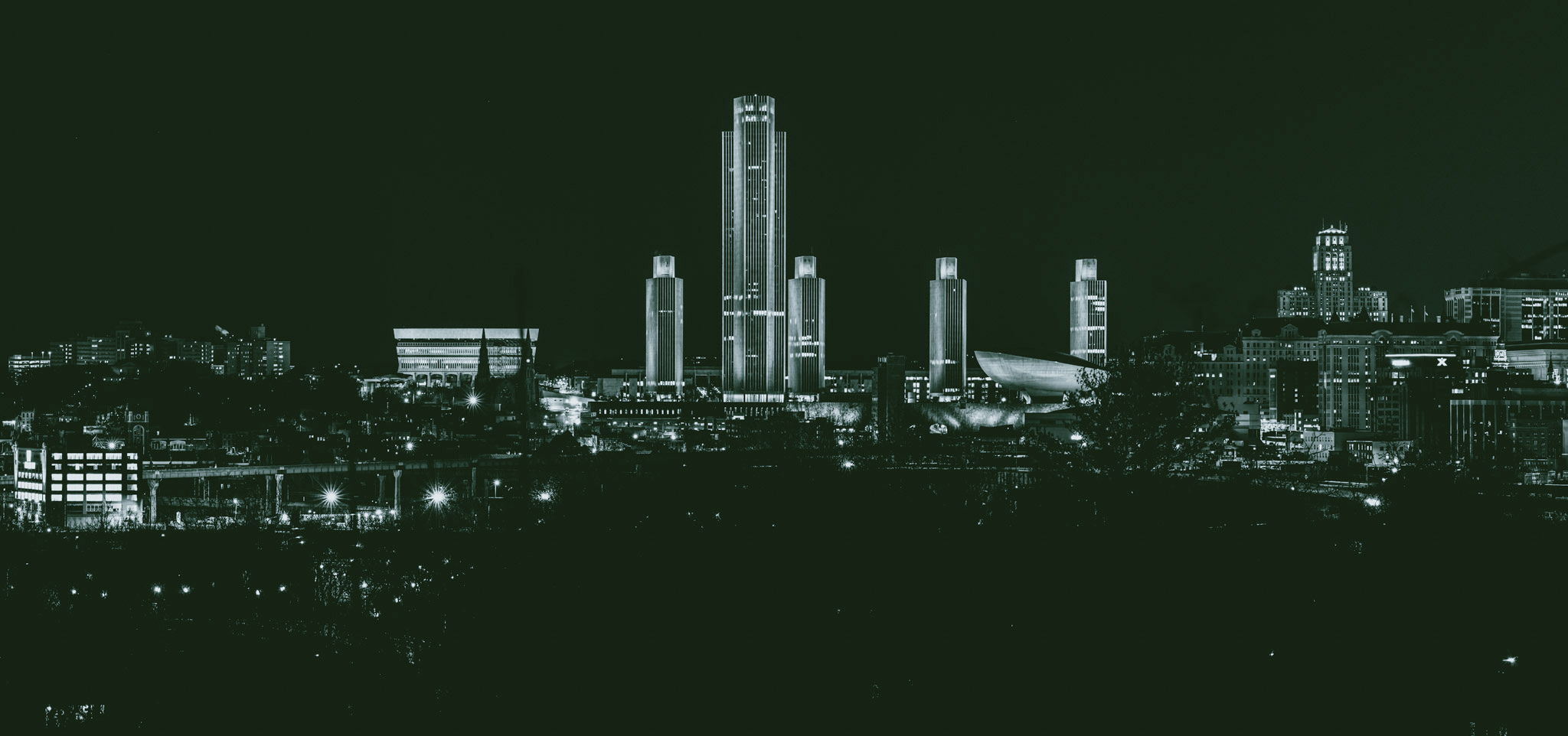 A panoramic view of a modern city skyline at night, featuring numerous illuminated skyscrapers.